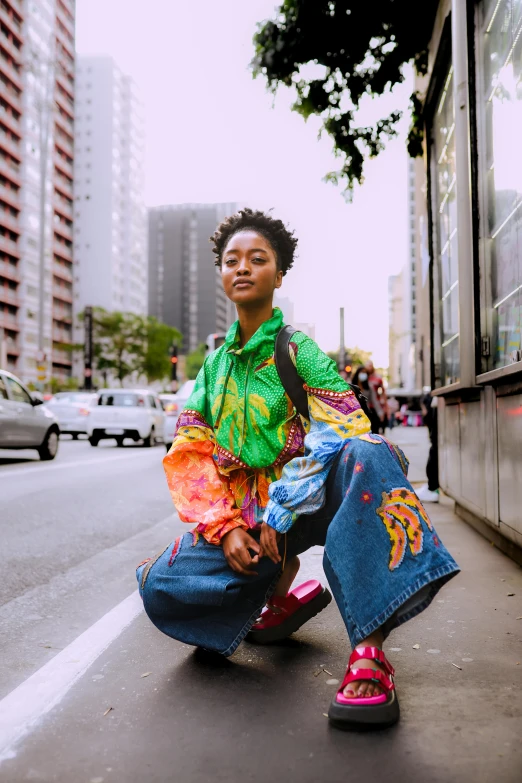 woman in oversized, multi - colored shirt crouching on the sidewalk