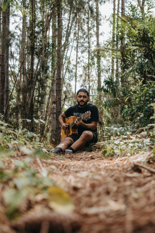 the young man is sitting in the woods with his guitar