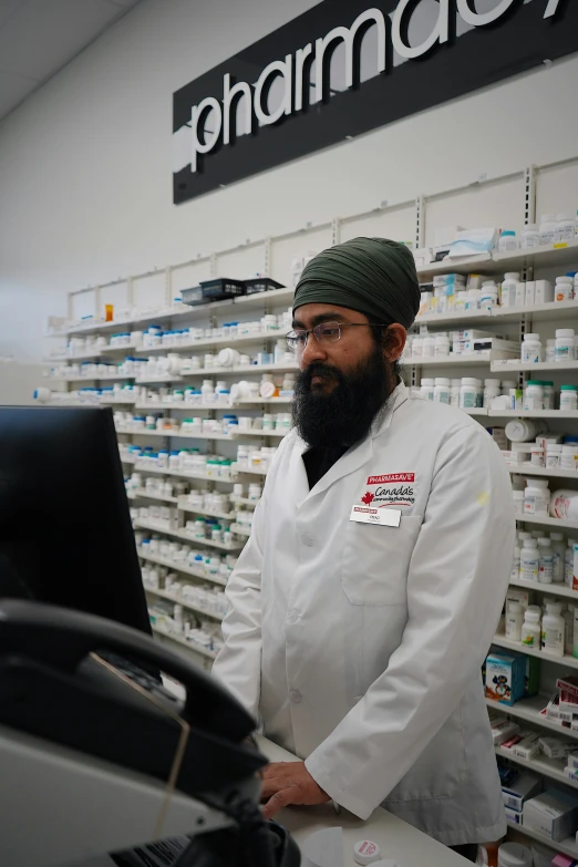 there is a male pharmian in the pharmacy and he is working on his computer