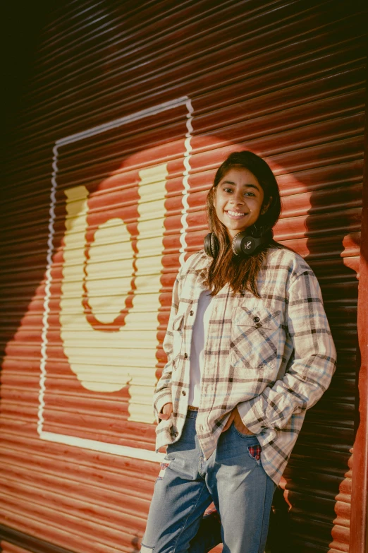 a woman standing against a red wall, with her hands in her pockets