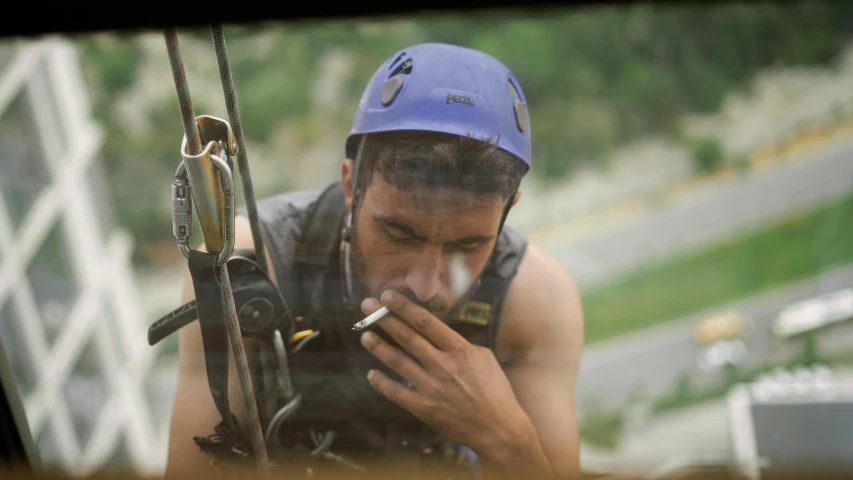 a man with a blue hat and a cigarette standing by a fence