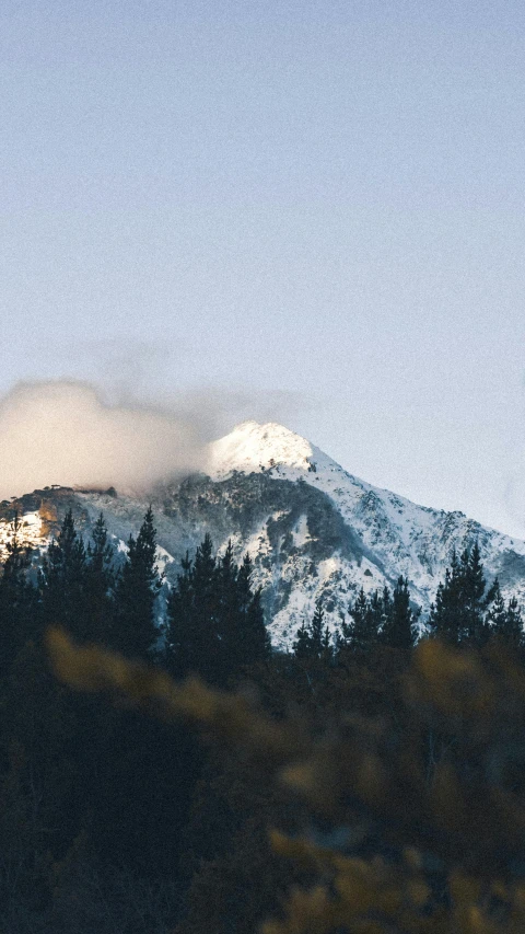 a snow covered mountain with clouds and trees