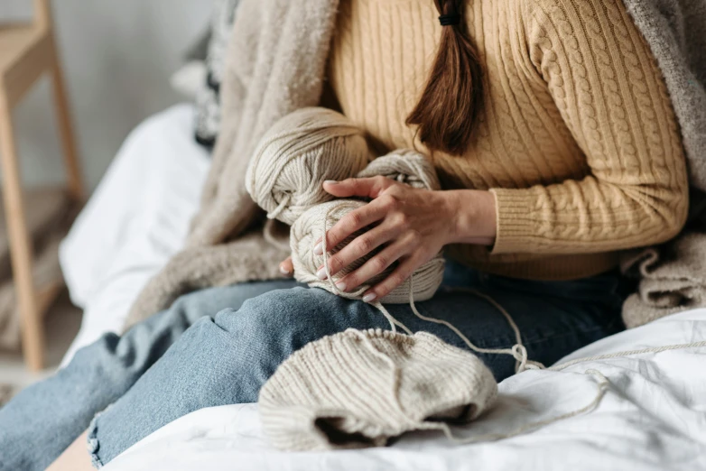 a woman sitting on a bed holding balls of wool