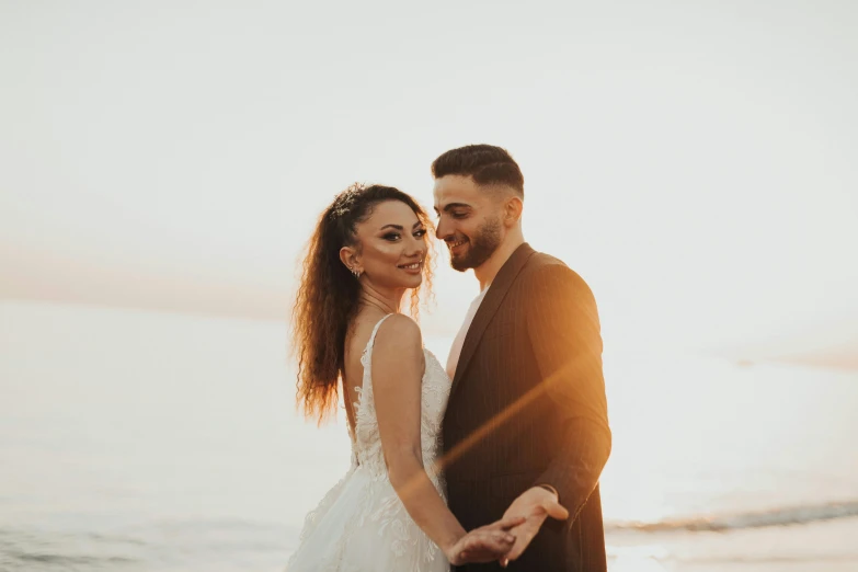 a young couple holds their hands out as they stand on the beach