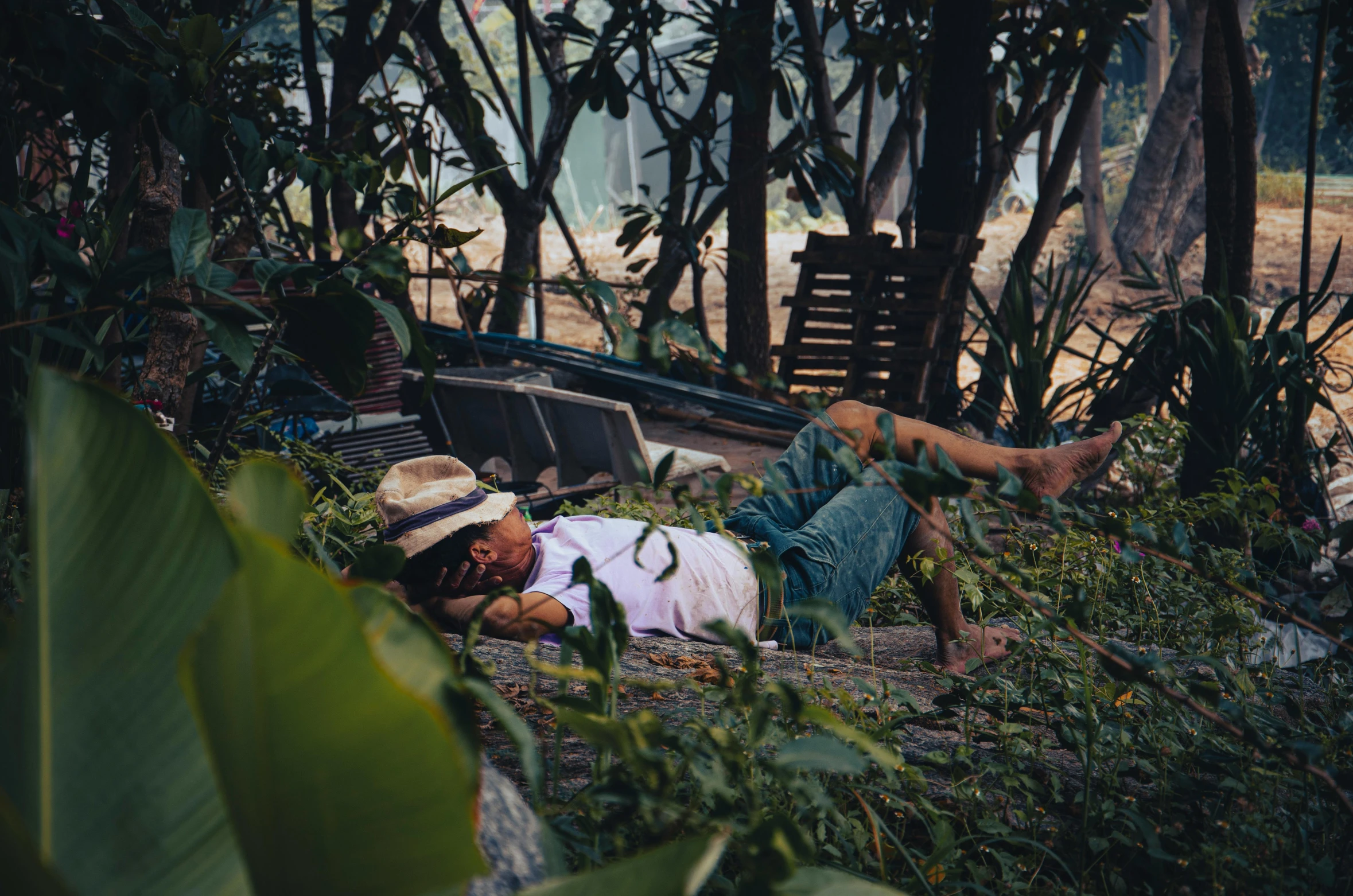 a man wearing hat lying on ground in forest