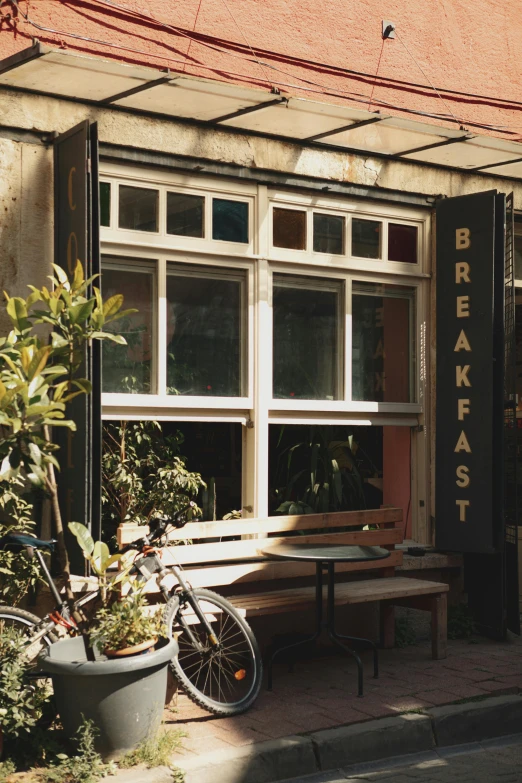 the front of a building with tables, plants and bikes parked outside