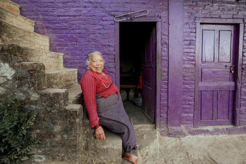 an elderly woman is sitting in front of her purple house