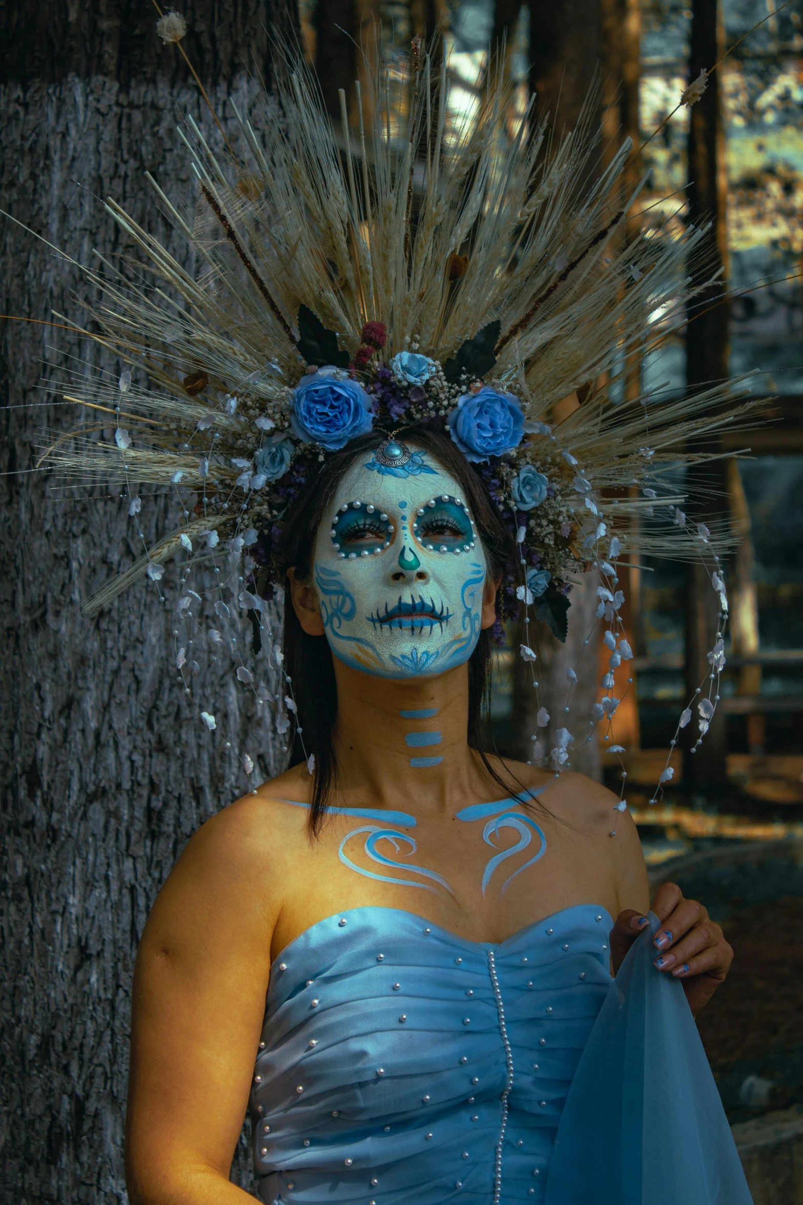 a woman with blue face paint on her body standing next to a tree