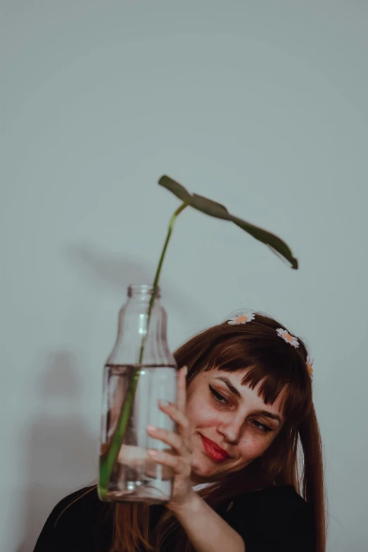 a woman holding a glass vase with a flower in it