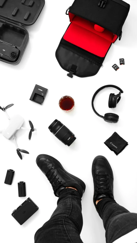 a person with their shoes out, a case, and various electronics laid out on the ground