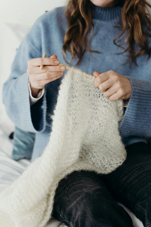 woman knitting while wearing black pants and blue sweater