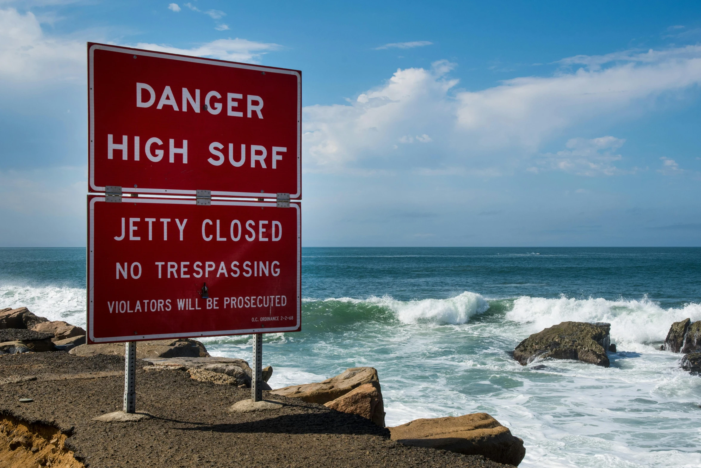 a red sign on the shore reads danger high surf