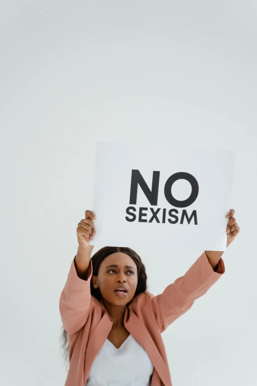 a woman is holding up a sign that says no sexism