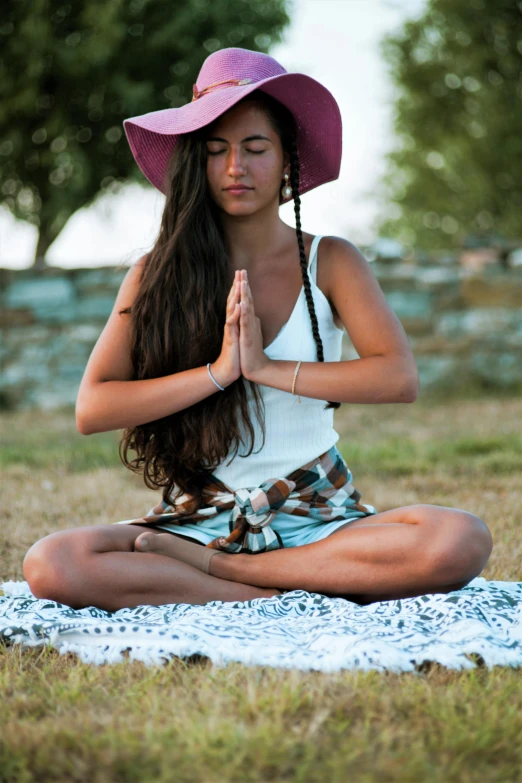 a young woman in a pink hat, sitting on a blue and white towel and wearing a pink hat