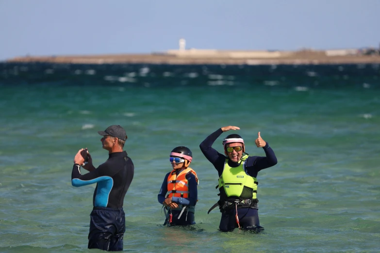 three people wearing wet suits standing in water waving