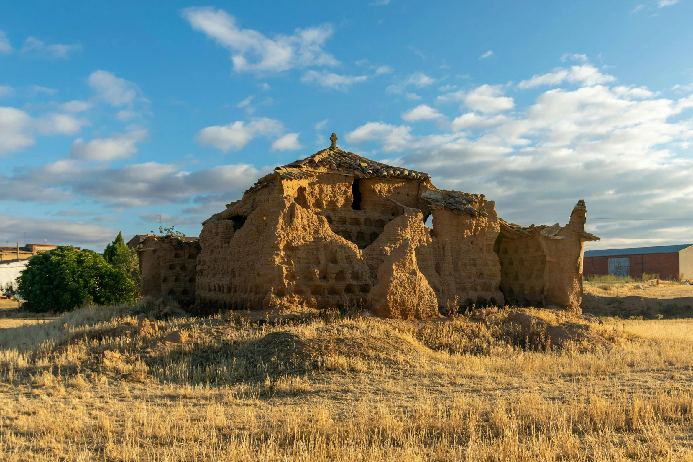 a field with very little grass and a old adobe structure