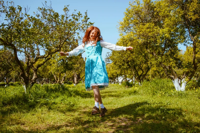 a girl in a dress stands in front of trees with her arms out