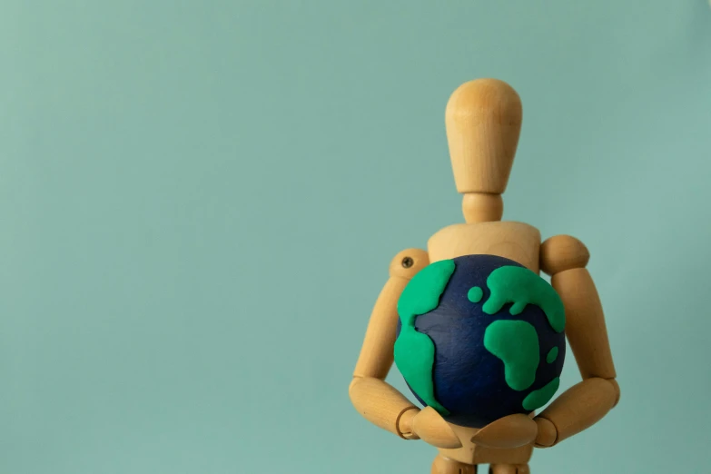 the wooden doll is holding up a green and blue globe