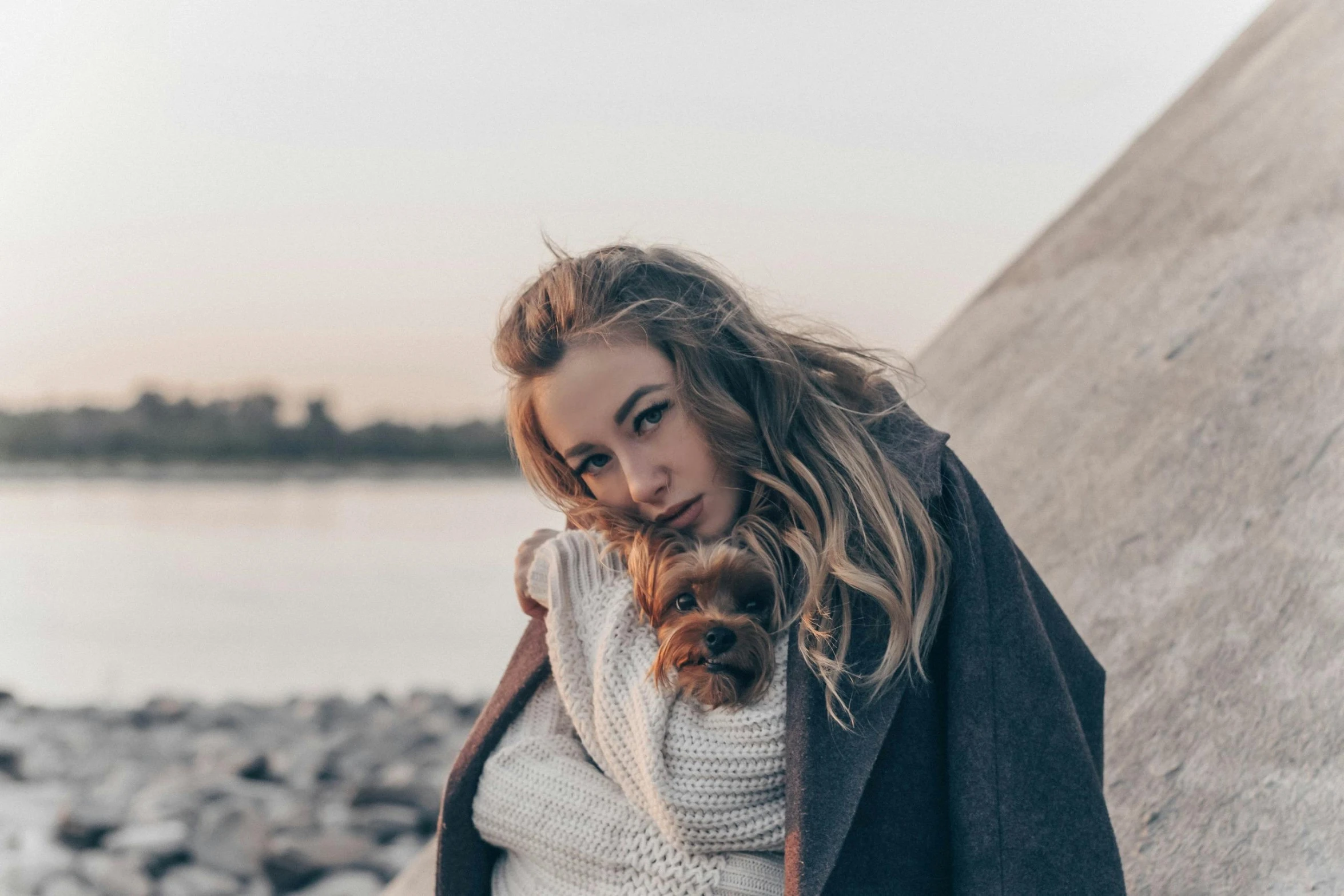 a beautiful young blonde woman wearing a white sweater and dark brown coat