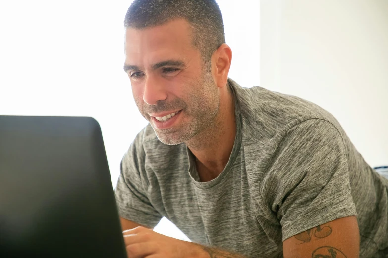 a smiling man sitting at his desk using a laptop