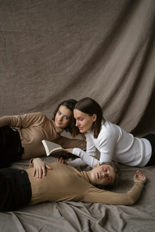 two women and a boy are laying on the ground while reading a book