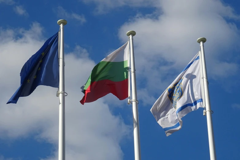 three flags flying in the wind in front of a cloud