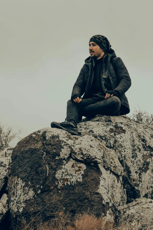 a man sitting on a rock wearing a black jacket and beanie