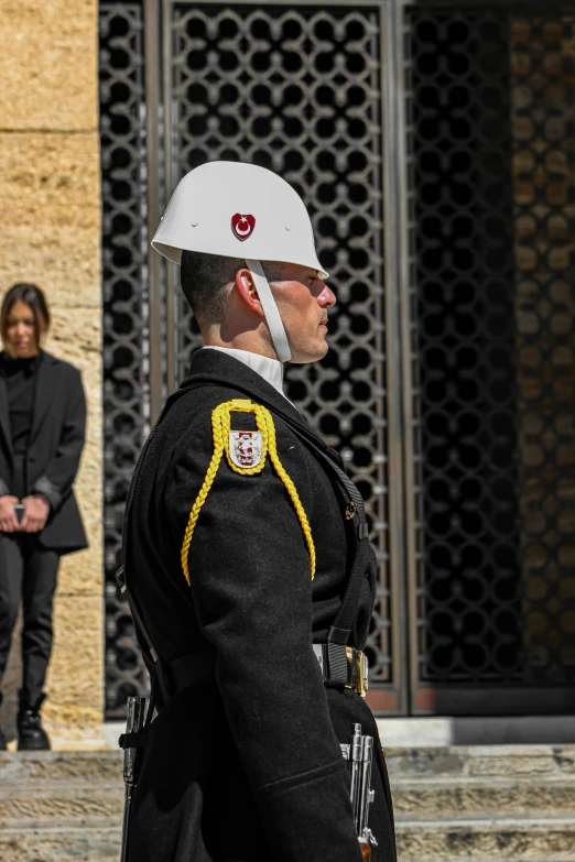 man in uniform and helmet stands with people standing behind him