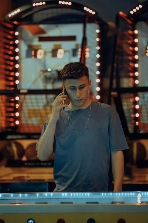a young man in a silver t - shirt is talking on a cellphone