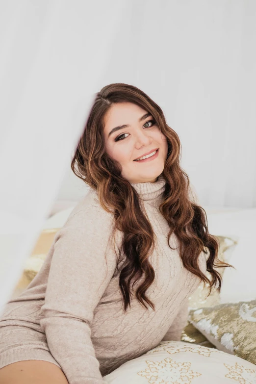 a woman sitting on a bed in a sweater