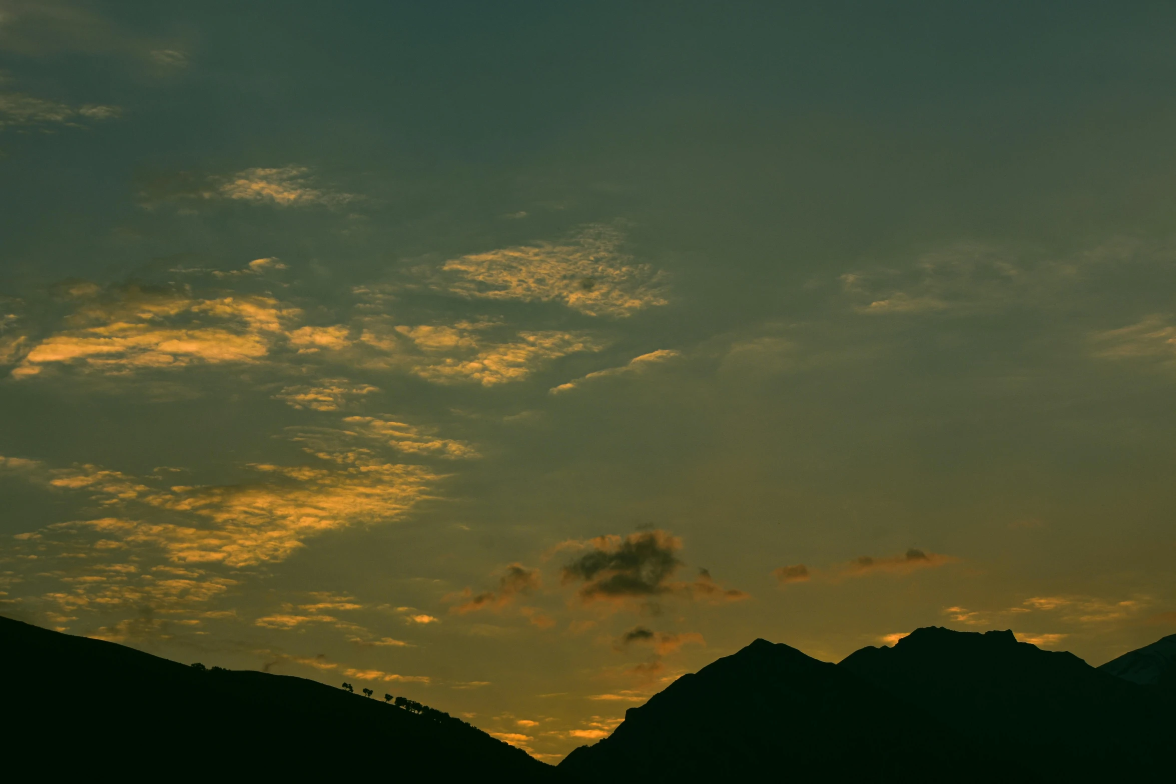 the silhouette of mountains are covered by a cloudy sky