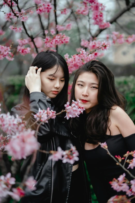 a couple of women standing next to each other under a pink flower covered tree