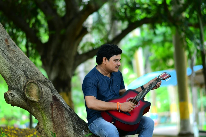 a man holding a red ukulele, sitting in a park