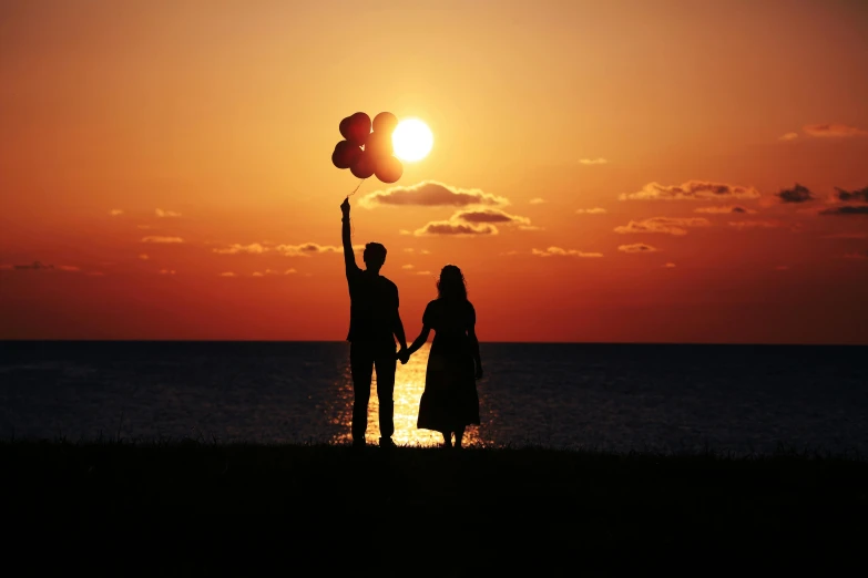 a silhouetted man and woman are holding up a kite