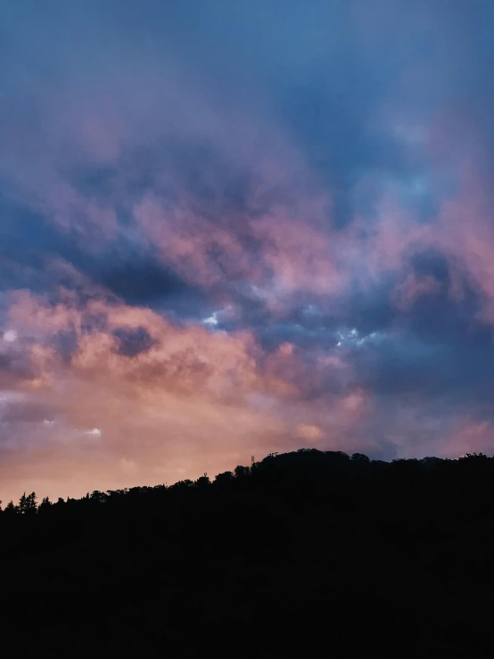 a blue and pink cloudy sky above a hill