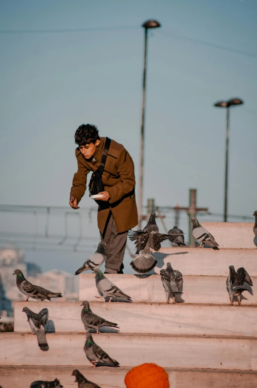 a man in brown jacket standing on a bunch of birds