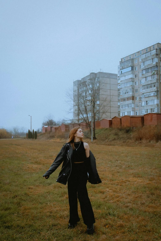 a young woman in an open grassy field with several tall buildings behind her