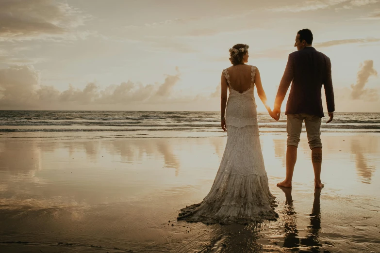 a couple holds hands while walking through water at sunset