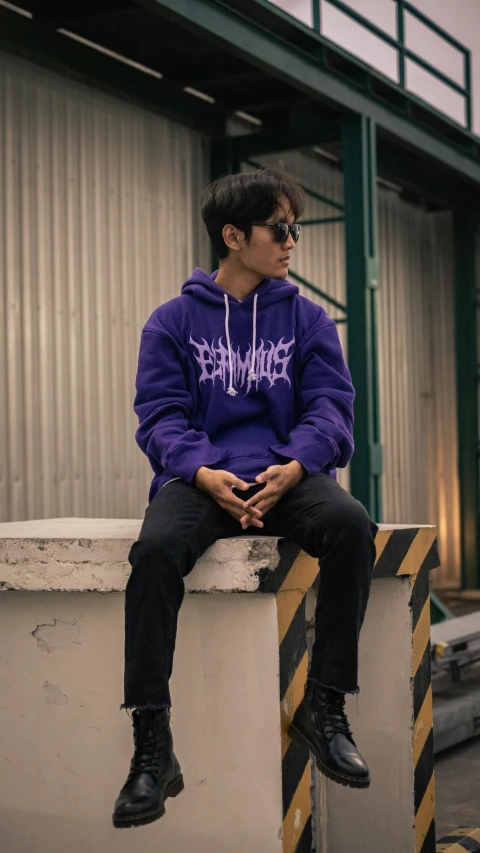 a man wearing a purple hoodie sitting on a piece of barricade