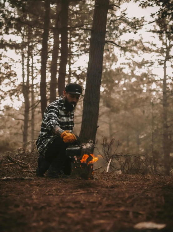 a man with safety gloves standing next to a burning campfire