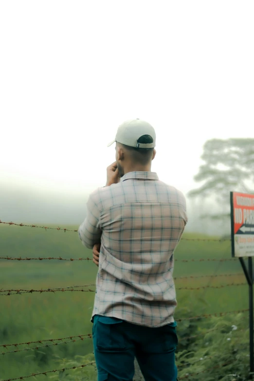 a man standing at a fence looking over a grassy field