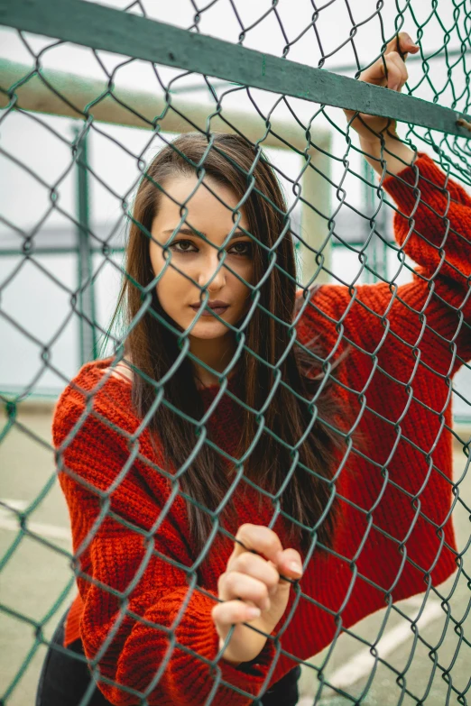 a girl standing behind a chain link fence in red