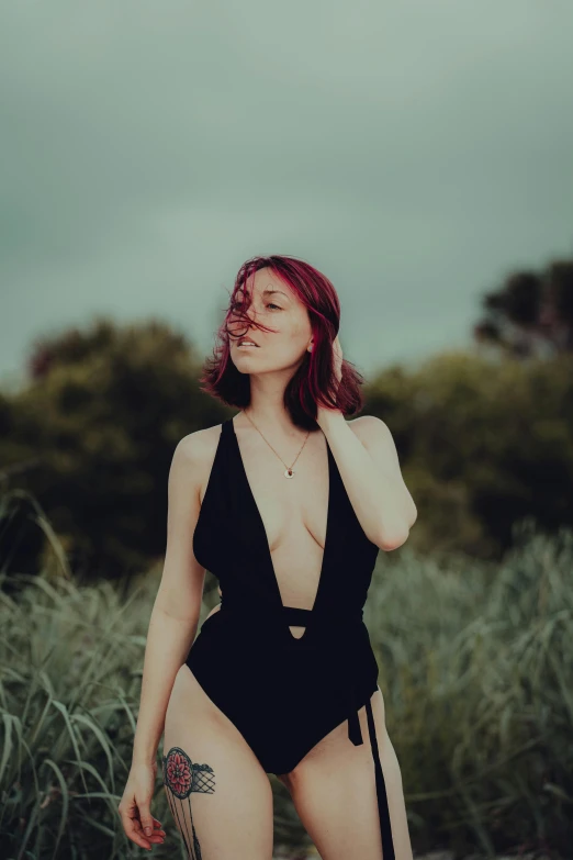 red haired woman in black swimsuit and tattoos, posing with her body painted with a tattoo