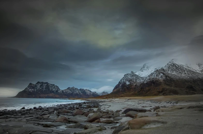 dark clouds hover over a mountain range and a body of water