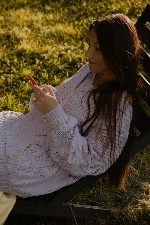 a woman is sitting in the grass with a cell phone