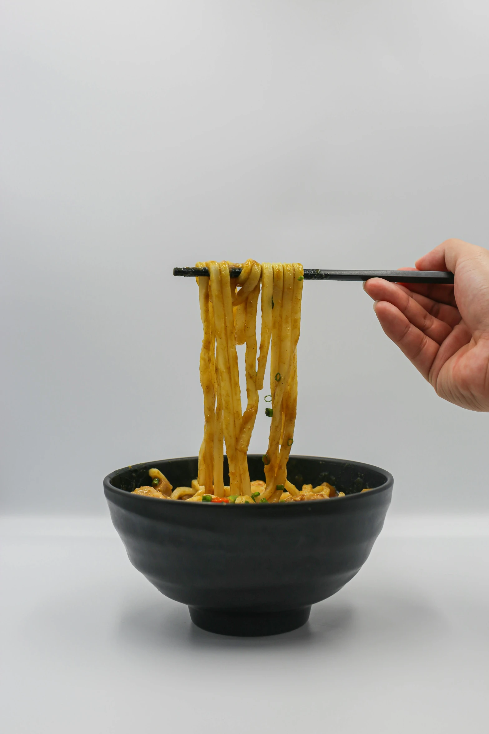 a hand is holding chopsticks over a black bowl filled with noodles