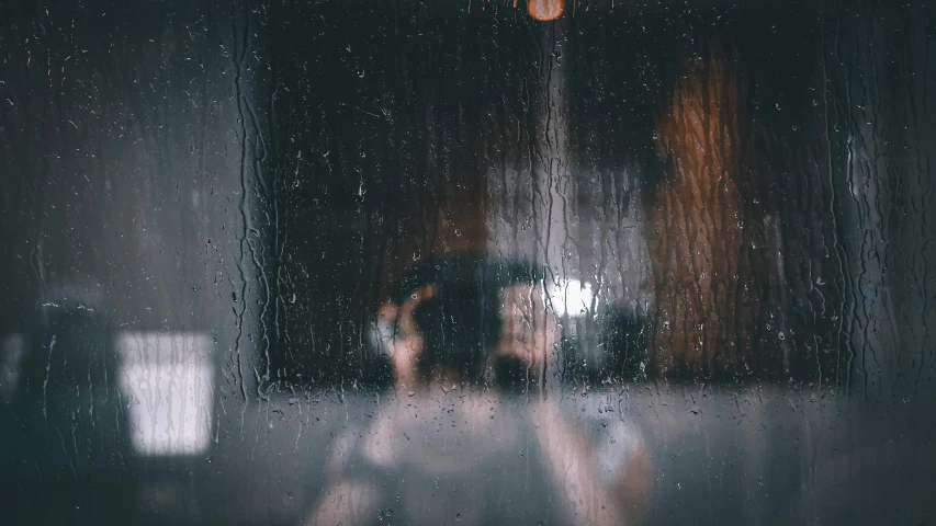 the person standing behind the rain soaked window