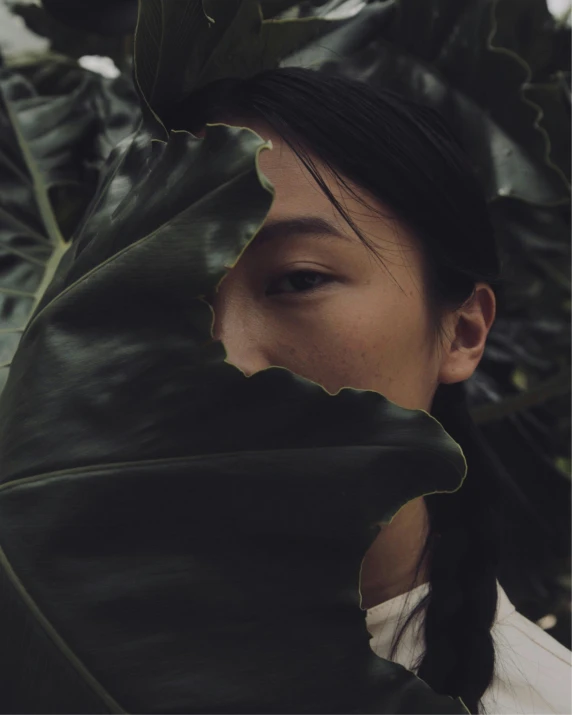 a woman standing under a large green leaf