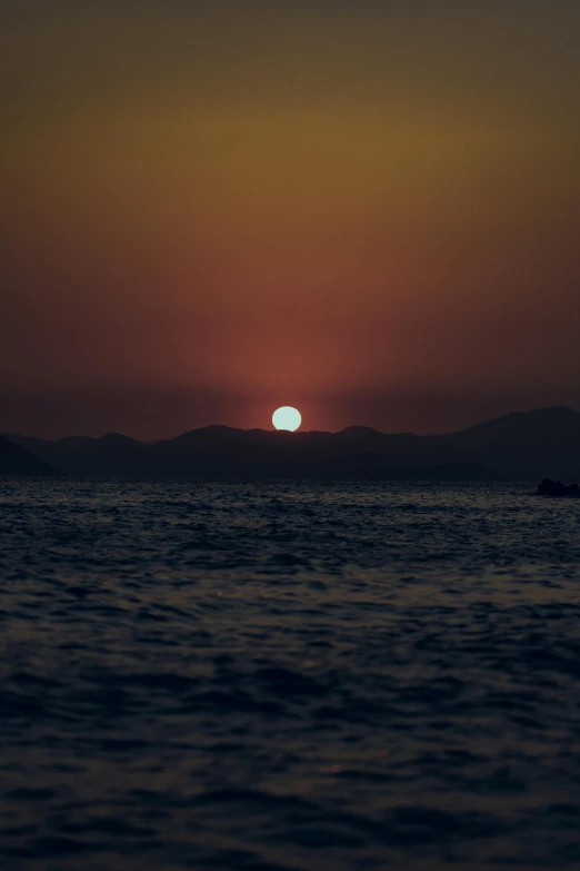 a sunset with the sun above water and mountains in the distance