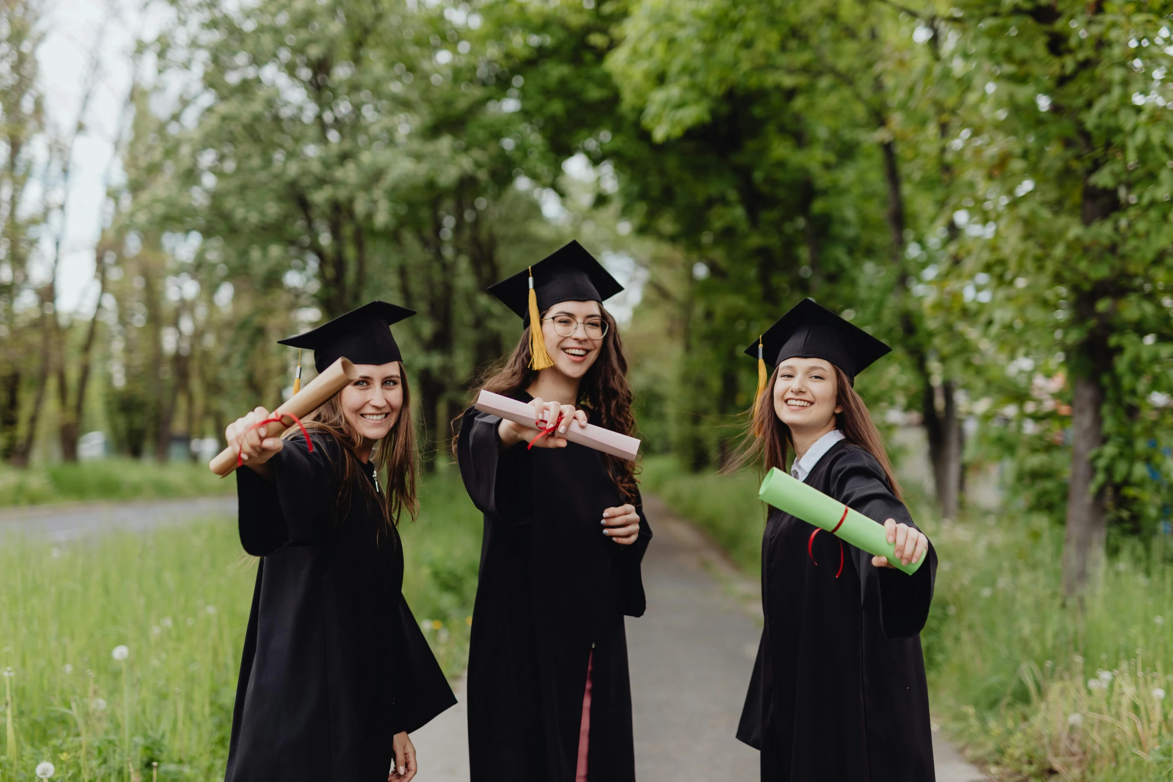 three girls in graduation robes and mortars on a path